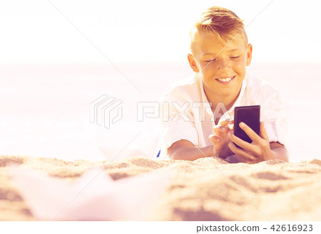 Boy looking at phone while resting on beach 42616923