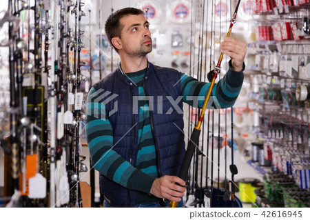 interested man choosing fishing rod for fishing in the sports shop 42616945