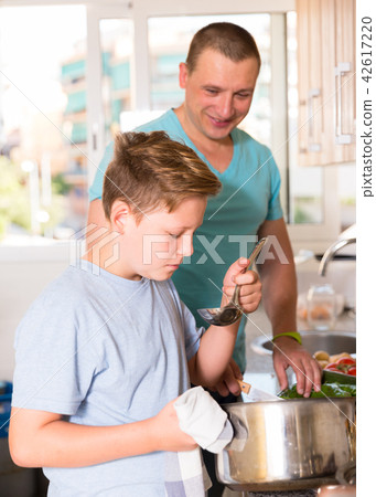 Man with his son are cooking soup in the kitchen Man with his son are cooking soup in the kitchen 42617220
