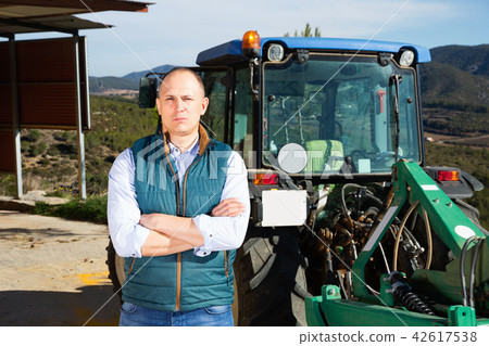 Confident male owner of vineyard posing near tractor outdoors in Confident male owner of vineyard posing near tractor outdoors in 42617538