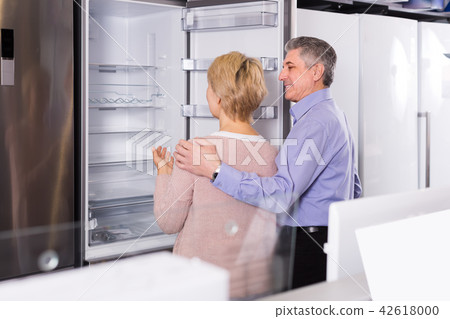 interested mature married couple in shop of household appliances are choosing home modern refrigerator interested mature married couple in shop of household appliances are choosing home modern refrigerator 42618000