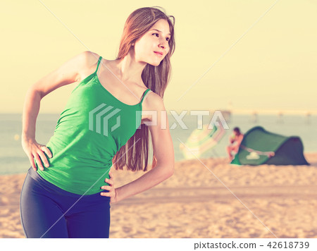 Smiling young woman in blue singlet is doing warm-up excercises Smiling young woman in blue singlet is doing warm-up excercises 42618739