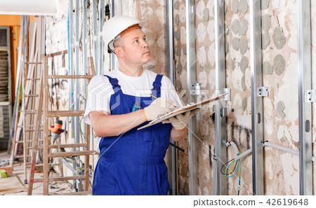 Focused construction worker inspecting room and planning upcoming repairs 42619648