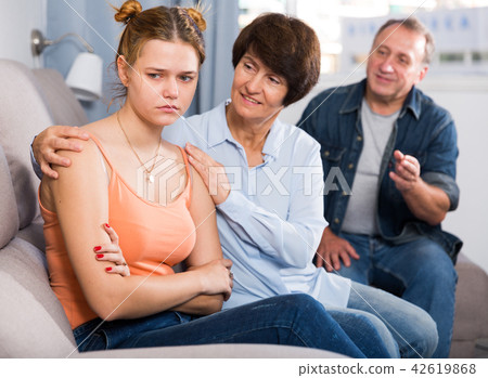 Adult couple is carefully talking with a sad daughter on sofa Adult couple is carefully talking with a sad daughter on sofa 42619868
