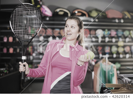admiring tennis female is choosing new rocket and ball for play in the store admiring tennis female is choosing new rocket and ball for play in the store 42620314