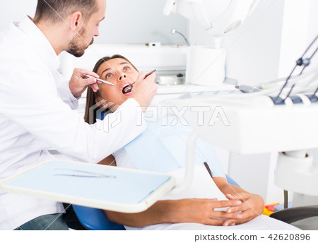 Dentist is treating woman patient which is sitting chair in clinic 42620896