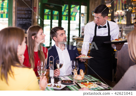 Man waiter is brings order to friends who have dinner and drink wine Man waiter is brings order to friends who have dinner and drink wine 42621041