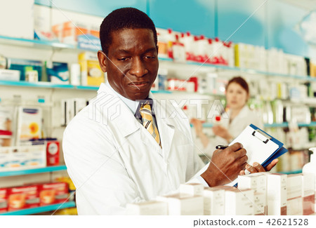 Professional male pharmacist working at drugstore, checking medicines inventory with female colleague 42621528