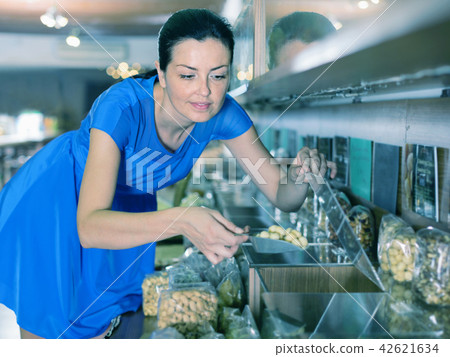 Woman taking nut by weight with scoop in organic shop Woman taking nut by weight with scoop in organic shop 42621634