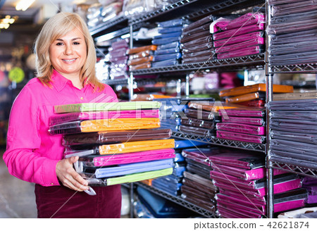 Portrait of mature woman showing stack of bedsheet in the textile shop Portrait of mature woman showing stack of bedsheet in the textile shop 42621874