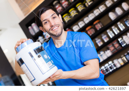 Smiling athletic guy seller showing pot of sport nutrition 42621897