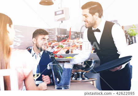 waiter bringing ordered seafood dishes to smiling couple 42622095