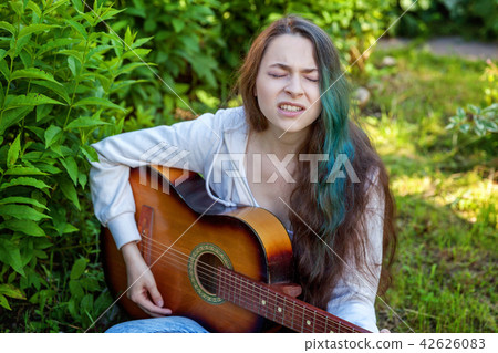 Young woman sitting in grass and playing guitar Young woman sitting in grass and playing guitar 42626083
