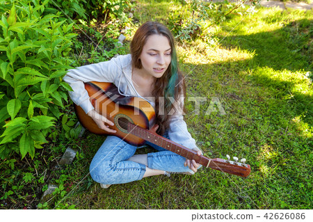 Young woman sitting in grass and playing guitar 42626086