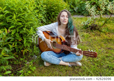 Young woman sitting in grass and playing guitar Young woman sitting in grass and playing guitar 42626096