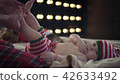 Cute baby boy dressed in striped christmas clothes is lying on beige bed and smiling while mother 42633492