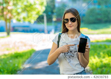 A teenage girl in her arms holds a smartphone. In summer in the park. Sunglasses. Free Space For 42638783