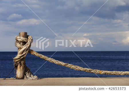 Rope knotted on wooden post in seafront, blue sea 42653373