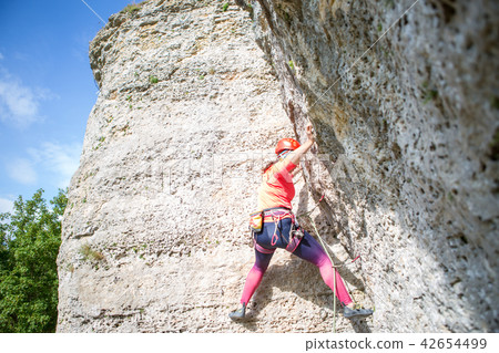 Photo from bottom of athletic woman in red helmet climbing a mountain 42654499