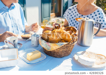 Two senior people having breakfast with bread basket on table in summer garden 42690326