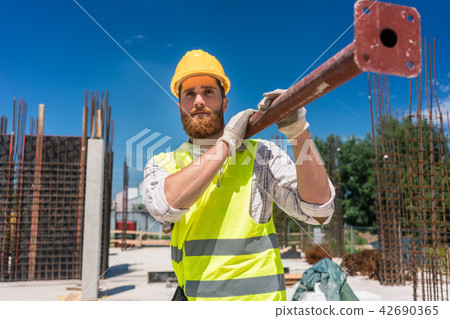 Blue-collar worker carrying a heavy metallic bar during work Blue-collar worker carrying a heavy metallic bar during work 42690365