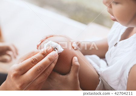 Parent helping child perform first aid knee injury Parent helping child perform first aid knee injury 42704211