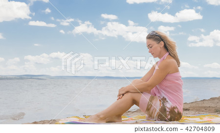 Attractive woman in a hat sits on the beach against the blue sea. Attractive woman in a hat sits on the beach against the blue sea. 42704809