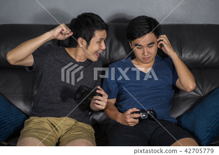 two man playing video games while sitting on sofa. win and lose two man playing video games while sitting on sofa. win and lose 42705779