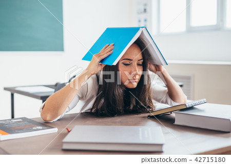 Tired woman sitting at the table and sleeping with book on head 42715180