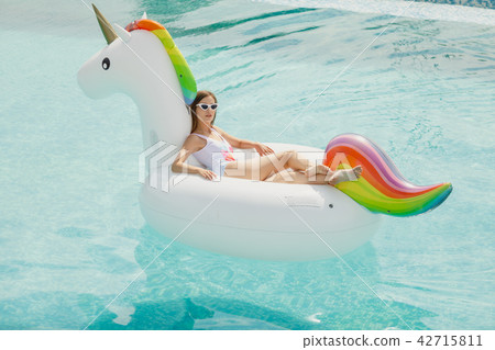 beautiful slim girl in a swimsuit. Floating on a big white beach inflatable unicorn pool beautiful slim girl in a swimsuit. Floating on a big white beach inflatable unicorn pool 42715811