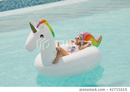 beautiful slim girl in a swimsuit. Floating on a big white beach inflatable unicorn pool beautiful slim girl in a swimsuit. Floating on a big white beach inflatable unicorn pool 42715819