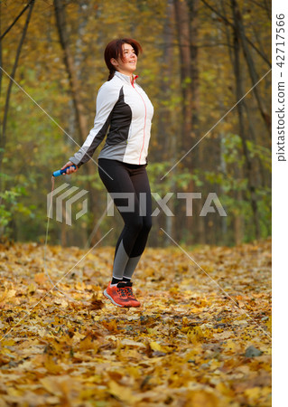 Photo of side view of sporty brunette jumping with rope at autumn forest 42717566