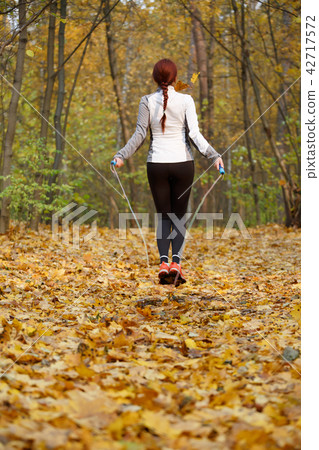 Photo from back of athlete woman jumping with rope at autumn forest Photo from back of athlete woman jumping with rope at autumn forest 42717572