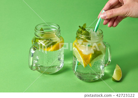 A woman's hand inserts plastic straw into a glass jar with lemonade from natural ingredients - water 42723122