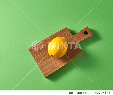 Ripe bright one yellow whole lemon on wooden board on a green background. Top view. 42723171