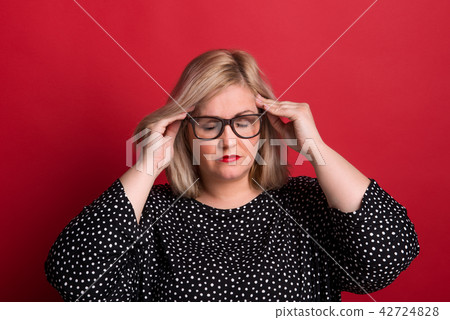 An overweight woman in studio, touching temples with her hands because of headache. 42724828