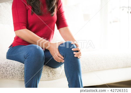 Woman sitting on sofa and feeling knee pain Woman sitting on sofa and feeling knee pain 42726331