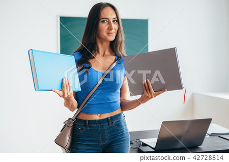 Female student in classroom holding book and smiling 42728814