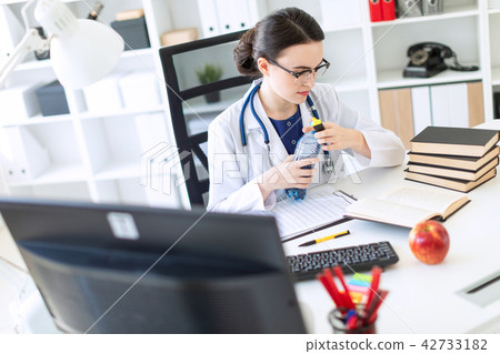 A beautiful young girl in a white robe sits at a computer desk, holds a marker in her hand and opens 42733182