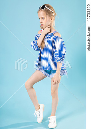 A girl in a T-shirt and shorts with glasses on her head is standing on a blue background. A girl in a T-shirt and shorts with glasses on her head is standing on a blue background. 42733390