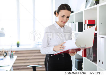 Young girl in the office near the rack and scrolls through the folder with the documents. 42733913