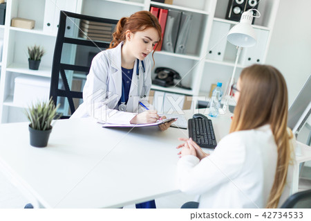 A beautiful young girl in a white robe is sitting at the desk in the office and communicating with A beautiful young girl in a white robe is sitting at the desk in the office and communicating with 42734533