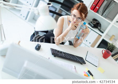 Beautiful young girl in the office working with documents, looking at the monitor and holding a Beautiful young girl in the office working with documents, looking at the monitor and holding a 42734534