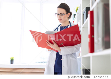 A beautiful young girl in a white robe is standing near the shelter and flips through a red folder 42734553