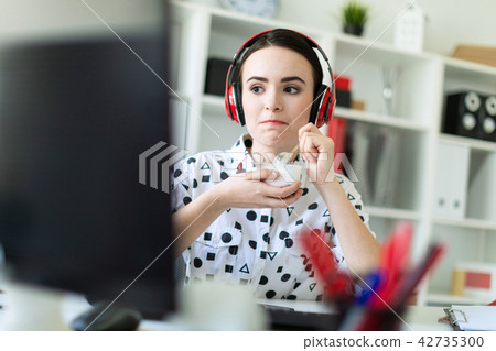 Beautiful young girl sitting in headphones at desk in office, eating yogurt and looking at monitor. 42735300