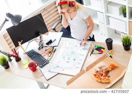 A young girl in the headphones stands near the table and holds a marker in her hand. On the table is A young girl in the headphones stands near the table and holds a marker in her hand. On the table is 42735607
