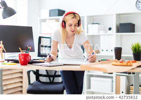 A young girl in the headphones stands near the table and holds a marker in her hand. On the table is A young girl in the headphones stands near the table and holds a marker in her hand. On the table is 42735612
