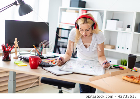 A young girl in the headphones stands near the table and holds a marker in her hand. On the table is A young girl in the headphones stands near the table and holds a marker in her hand. On the table is 42735615