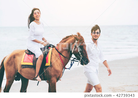 Young couple goes horse riding on tropical beach. Young couple goes horse riding on tropical beach. 42739343
