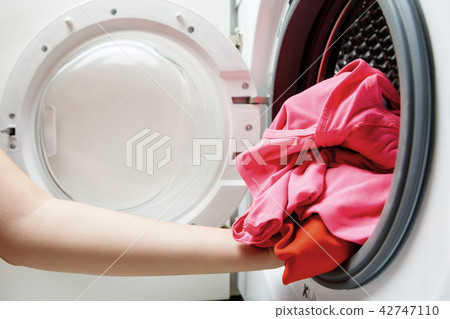 Photo of woman hands folding things in washing machine Photo of woman hands folding things in washing machine 42747110